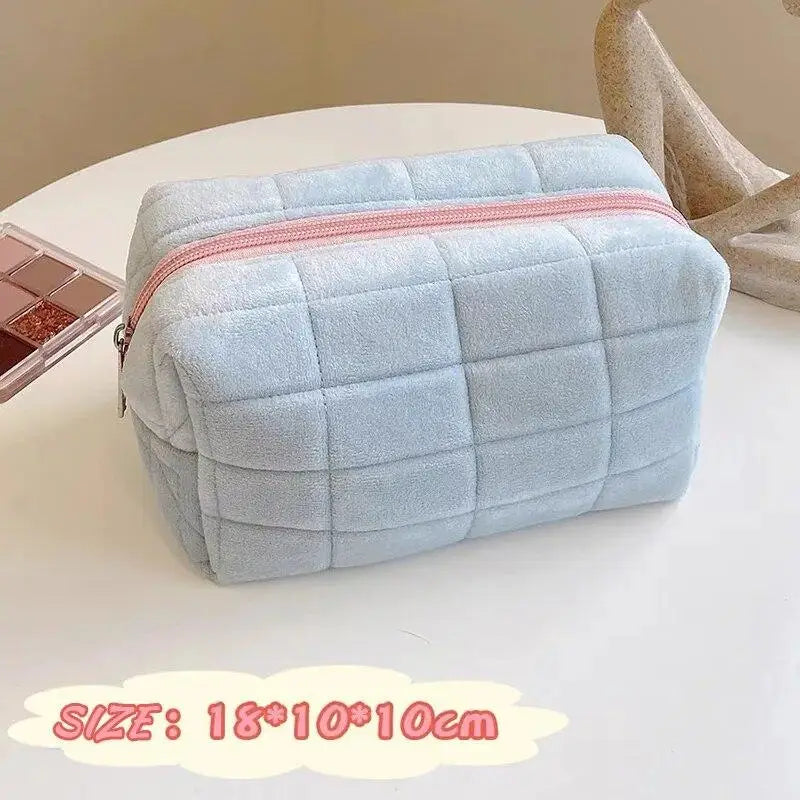 Light blue quilted portable makeup bag with a pink zipper on a white surface.