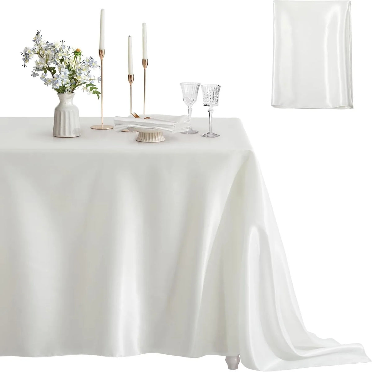 A white satin tablecloth set for dining featuring tall candles, glassware, and a floral centerpiece.