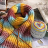 A close-up of colorful gradient cake yarn in various shades of purple, blue, yellow, and orange, displayed for knitting or cr