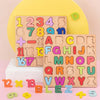 A wooden alphabet number and shape puzzle board with various letters, numbers, and shapes scattered on a pink surface.