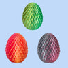 Three 3D printed dragon egg figurines in green, red, and dark gray on a light blue background.