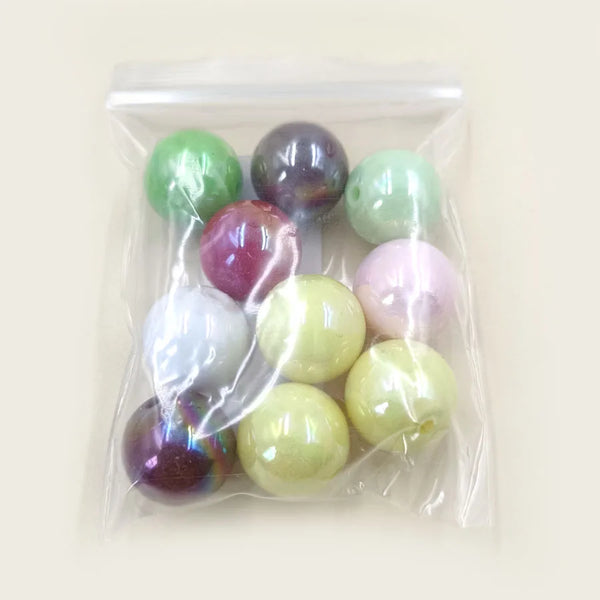 A clear plastic bag contains various iridescent and solid colored acrylic beads for jewelry making.