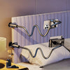 A silver curved stand designed to hold a tablet or phone, positioned next to a bed.