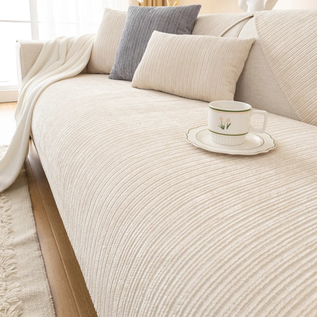 A beige sofa with light neutral cushions and a white cup on the fabric.