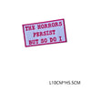 A pink embroidered letter patch with black text that reads The Horrors Persist But So Do I