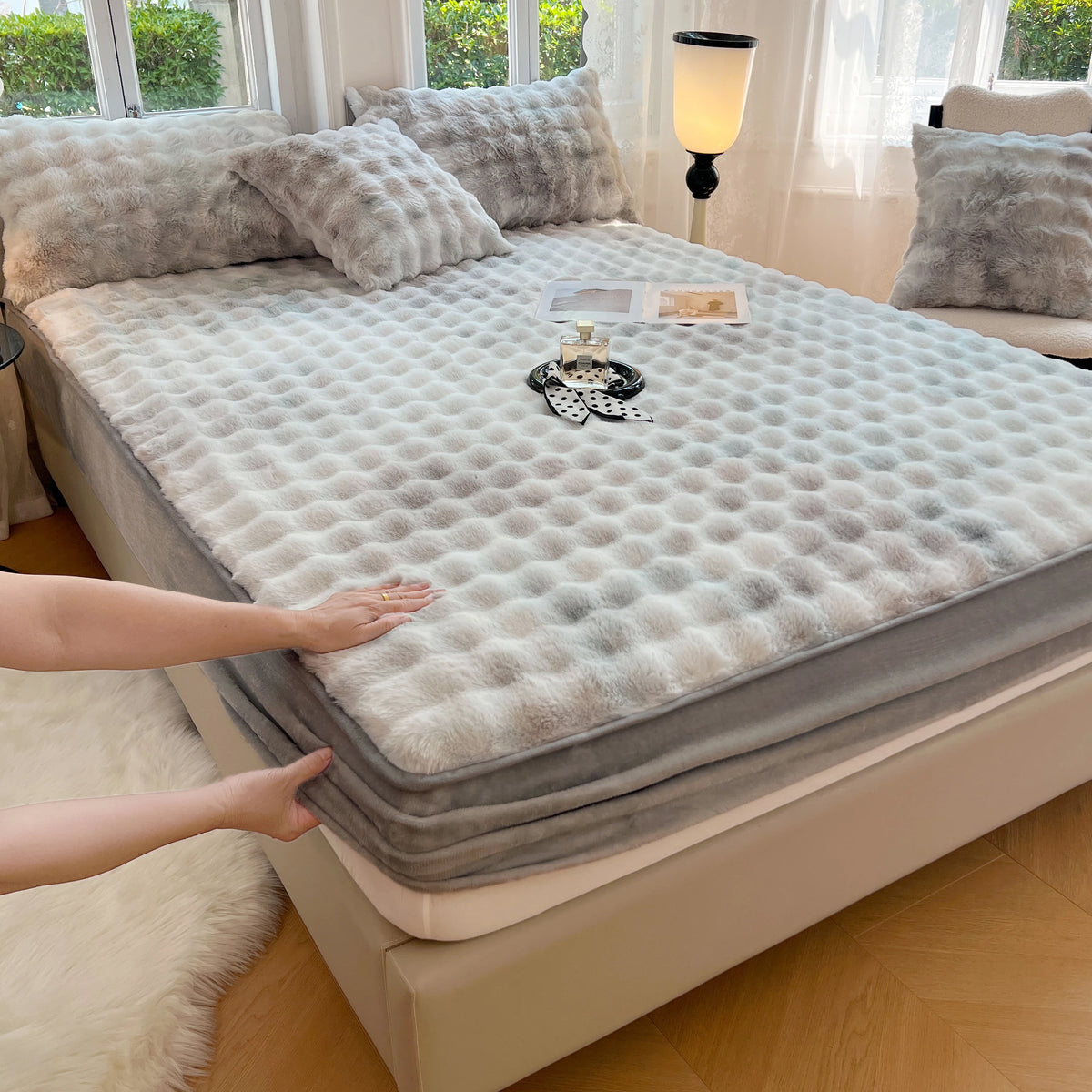 A luxury faux fur fitted sheet and pillowcase set displayed on a bed, with a hand touching the fabric.