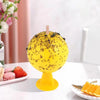 A yellow sticky fruit fly trap ball with black specks is displayed on a white surface.