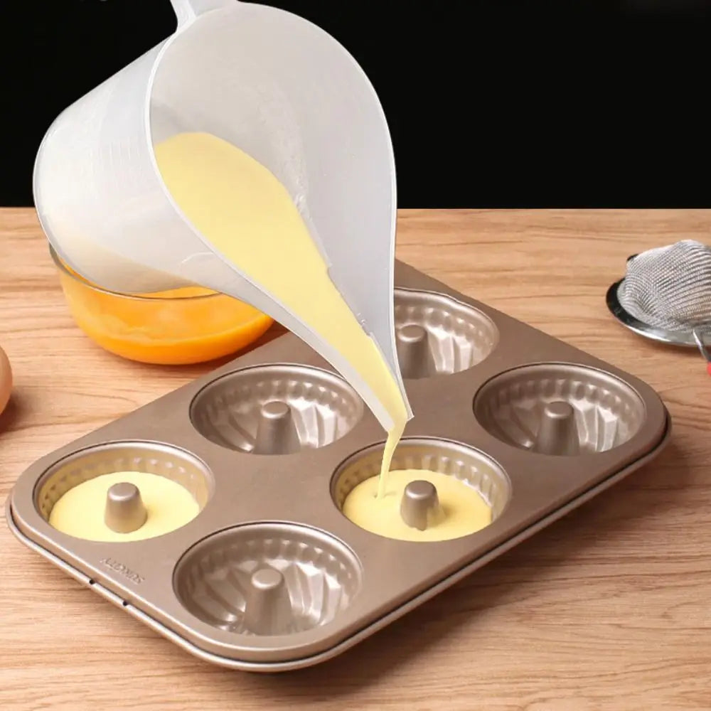 A white plastic measuring cup with a long spout pours yellow liquid into multiple small molds.