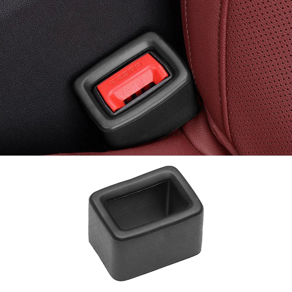 A black protective cover for a car seatbelt buckle with a red release mechanism shown against a dark fabric background.
