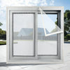 A modern window frame with a self-adhesive mesh screen installed, showing an outdoor landscape view.