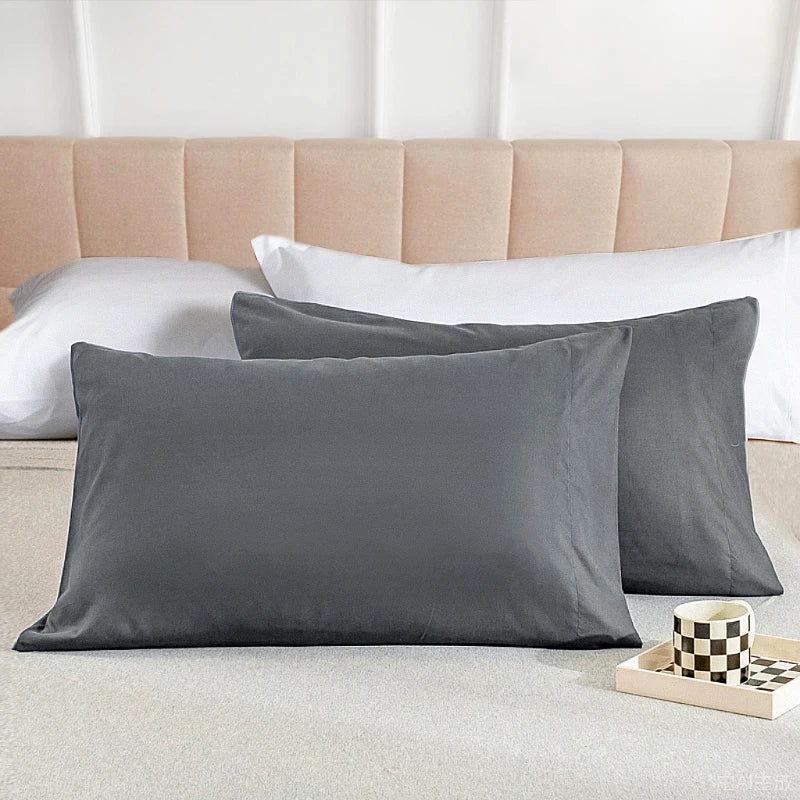 A set of two gray microfiber pillowcases resting on a light-colored bed with a beige headboard.
