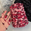 A close-up of a skein of hand-dyed variegated yarn in shades of pink and maroon resting on a hand.