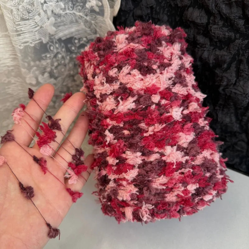 A close-up of a skein of hand-dyed variegated yarn in shades of pink and maroon resting on a hand.