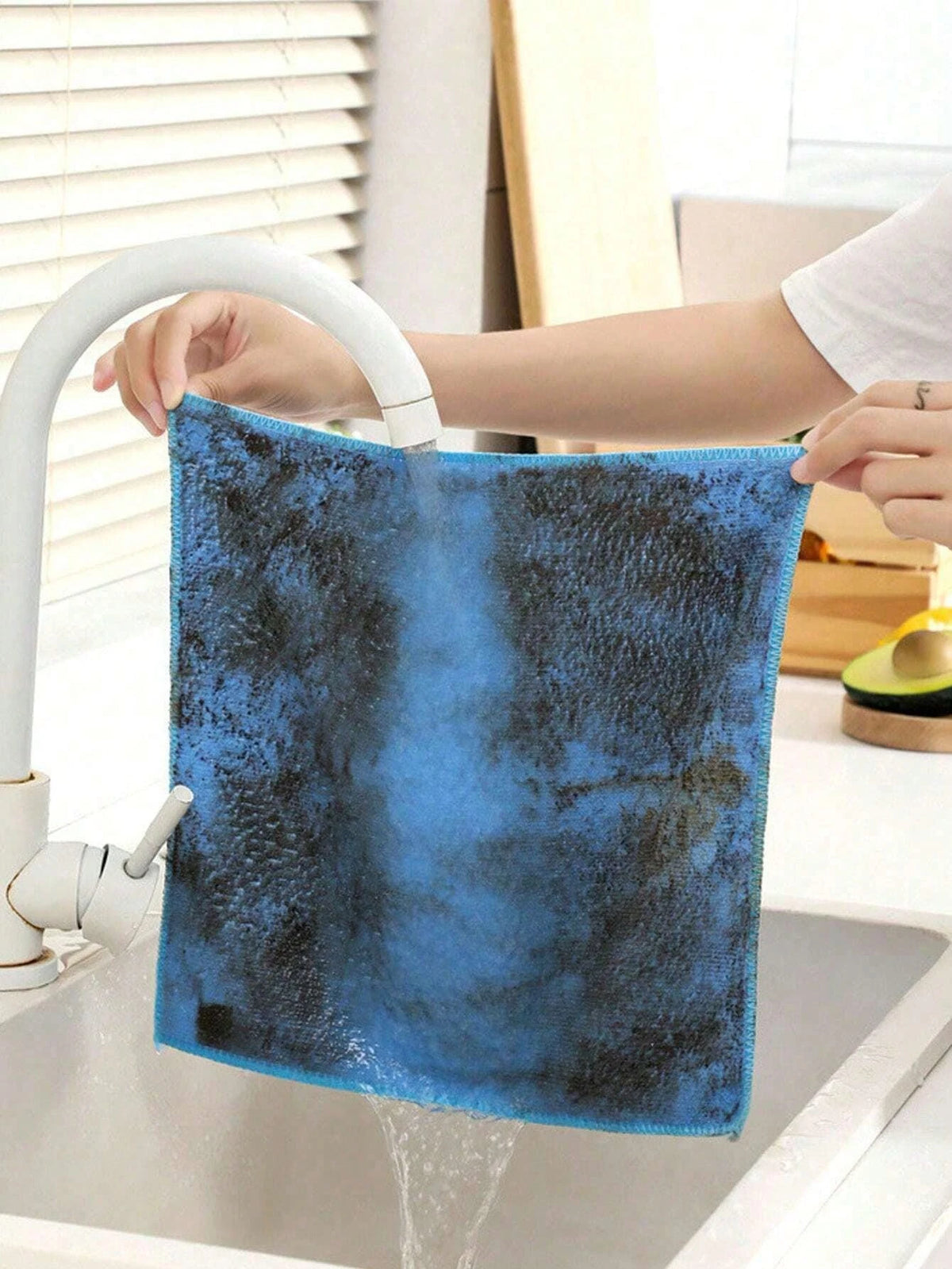 A blue microfiber cleaning cloth is being rinsed under a faucet in a kitchen sink.