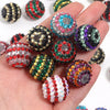 A hand holds a set of five resin rhinestone beads with two-tone striped designs in various colors and shades.