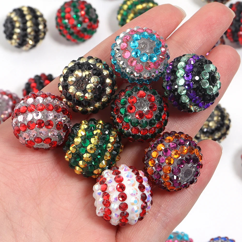 A hand holds a set of five resin rhinestone beads with two-tone striped designs in various colors and shades.