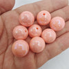 Several small, round, translucent peach-colored acrylic beads with holes are held in a person's hand.