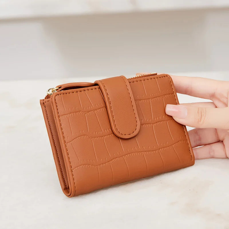 A tan leather compact zippered wallet with a quilted pattern is held in a hand on a light surface.
