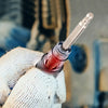 A hand holds an automotive spark plug ignition tester with a diagnostic gauge, showing the metal plug tip.