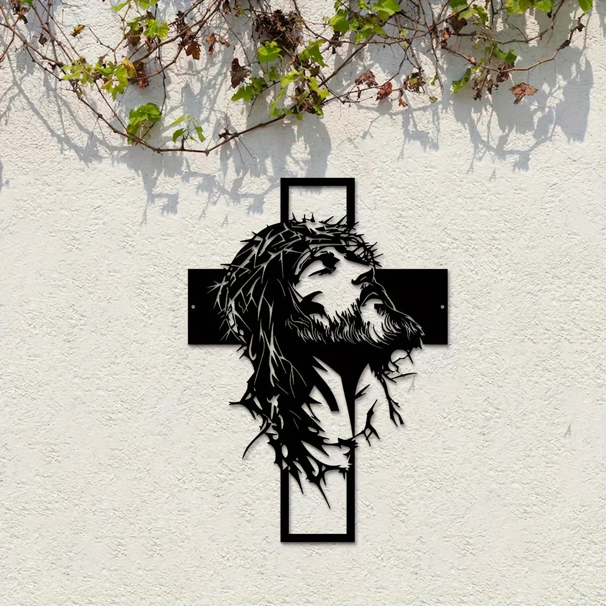 Silhouette noire de la tête et de la barbe de Jésus dans une croix montée sur un mur blanc.