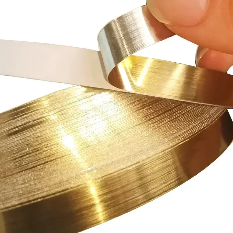 A hand is holding a roll of gold-colored self-adhesive waterproof tile gap sealing tape.