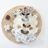 A stack of six patterned cotton baby feeding bibs resting on a woven mat.