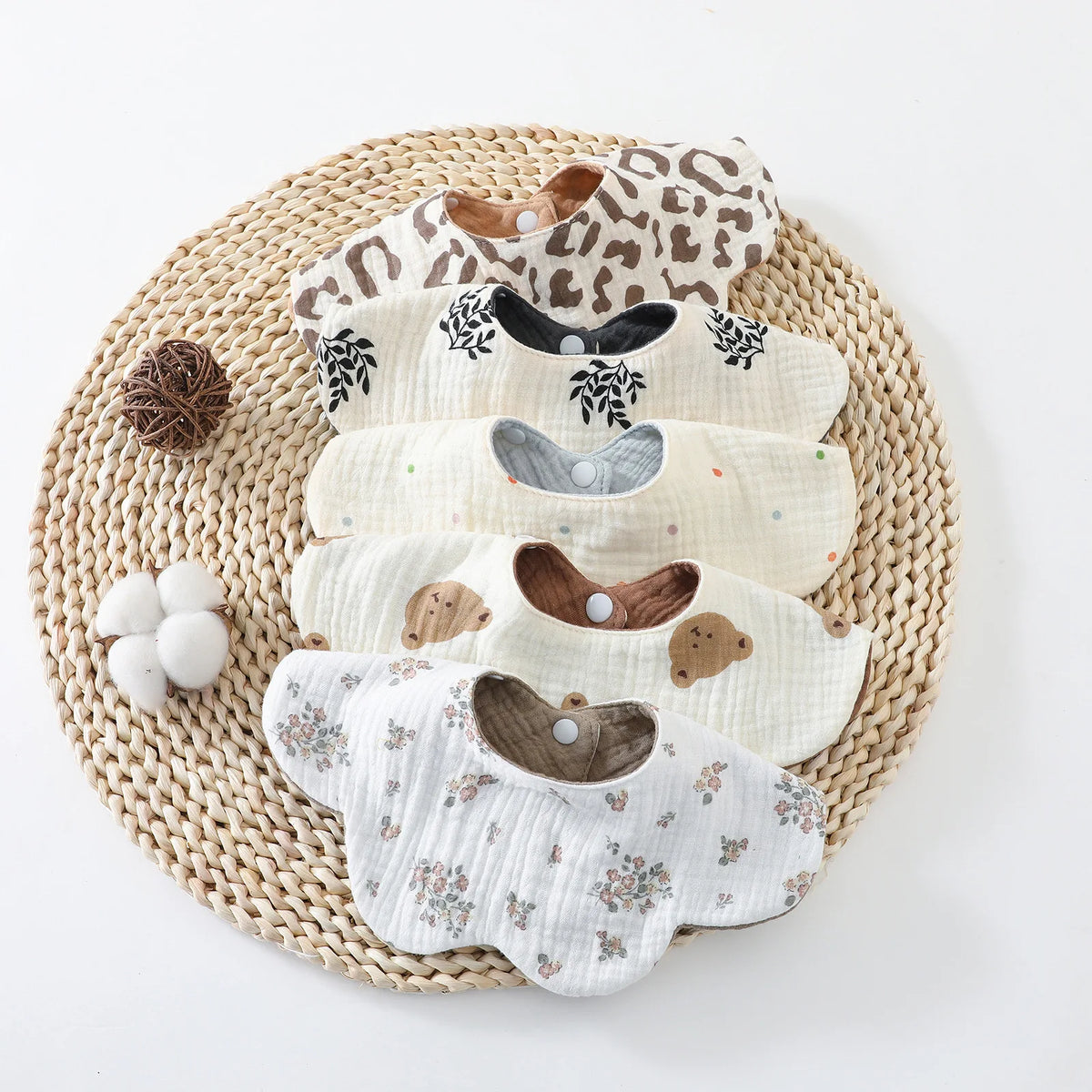 A stack of six patterned cotton baby feeding bibs resting on a woven mat.