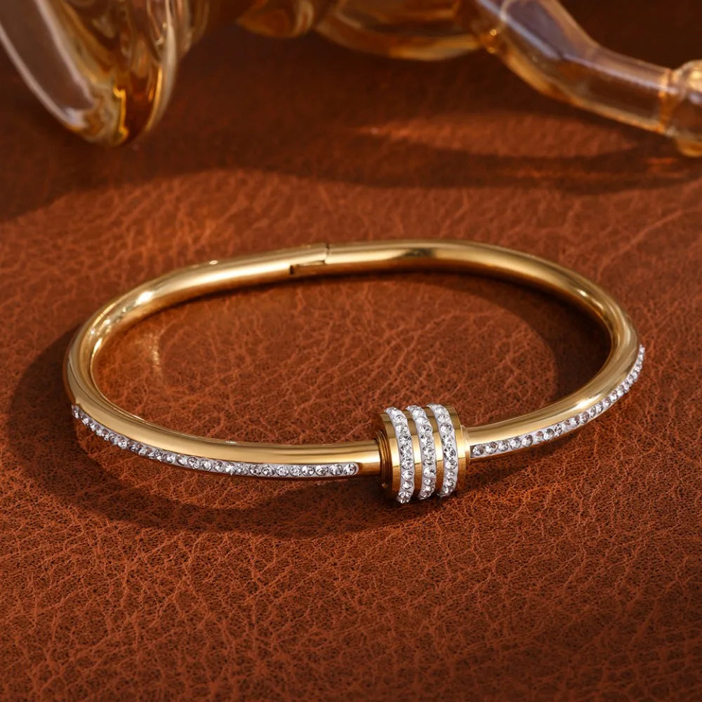 A gold stainless steel four-leaf clover bracelet with cubic zirconia stones resting on brown leather.