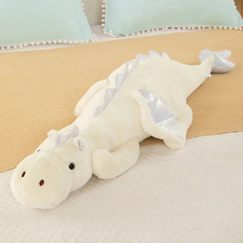 A white dragon plush pillow with silver accents resting on a beige surface.