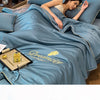 A woman rests on a blue comforter featuring the Dreamcity embroidery, highlighting the ultra-soft cooling fabric.