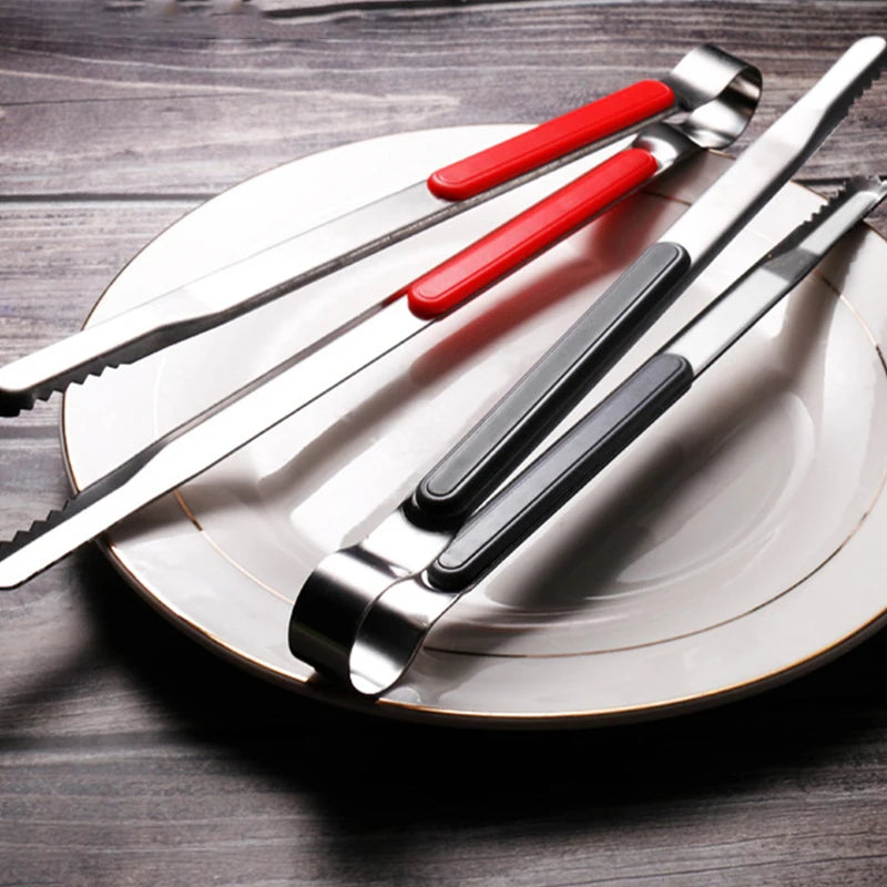A set of premium stainless steel BBQ tongs resting on a white plate on a dark wooden surface.