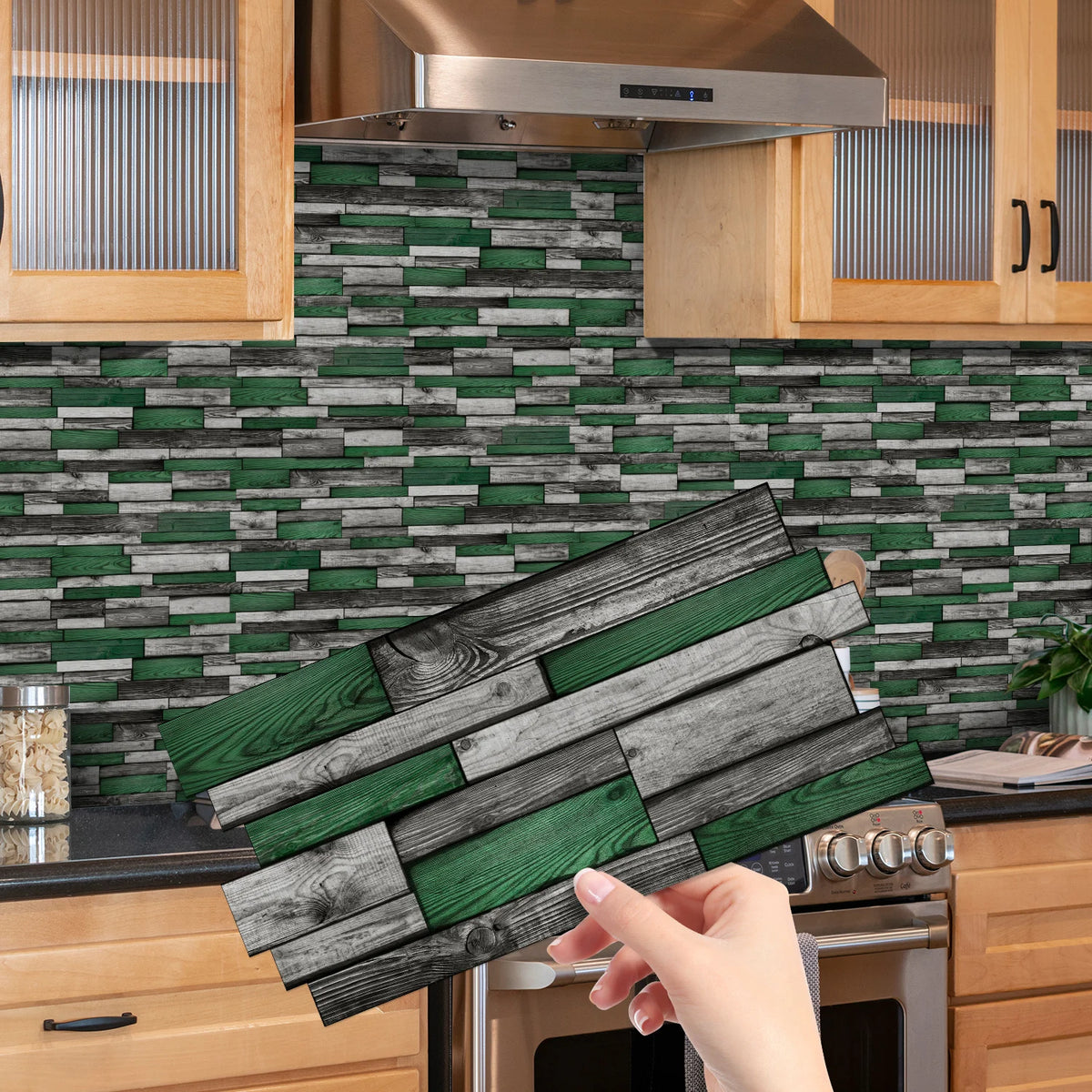 A hand holds a rectangular peel-and-stick tile sticker featuring a distressed green and gray wood plank pattern for a kitchen