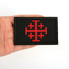 A black embroidered patch featuring a red Knights Templar cross shield design on a hand.