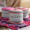 A stack of colorful gradient cake yarn spools resting on a pink knitted fabric.