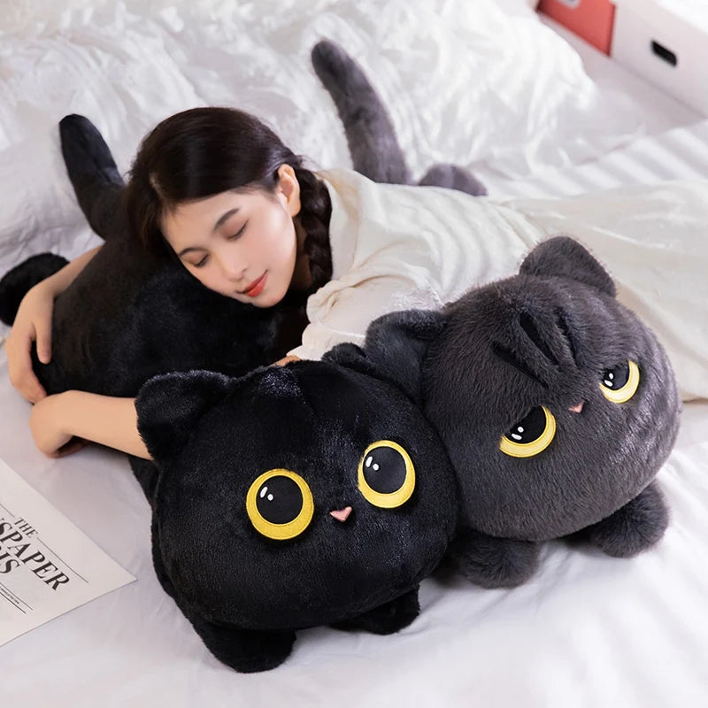 A person is cuddling a soft black cat plush toy on a white bed.
