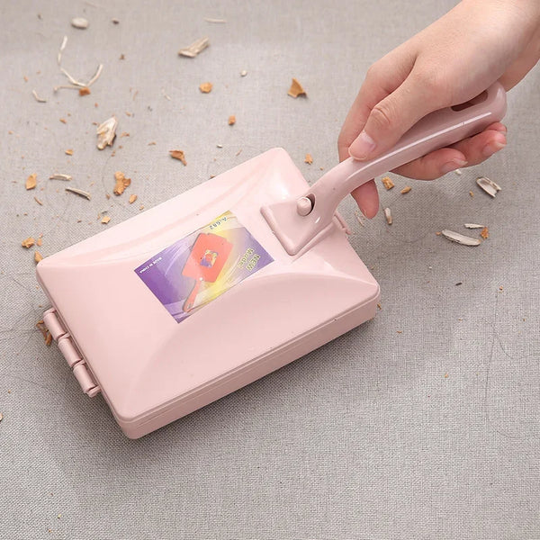 A hand holds a pink handheld double roller brush used for pet hair and debris removal on a gray surface.