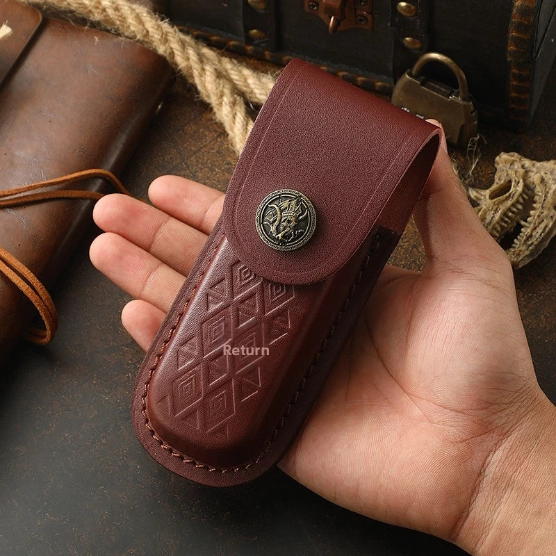A hand holds a dark brown leather folding knife case with a decorative metal emblem.