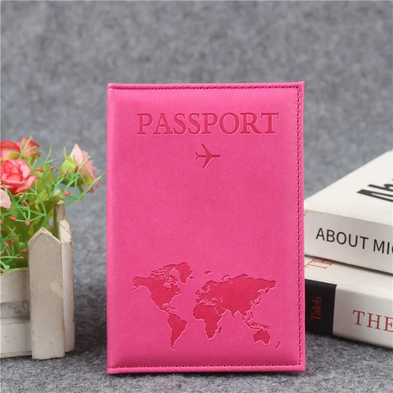A pink passport holder with a silver airplane and world map design resting on a gray surface.