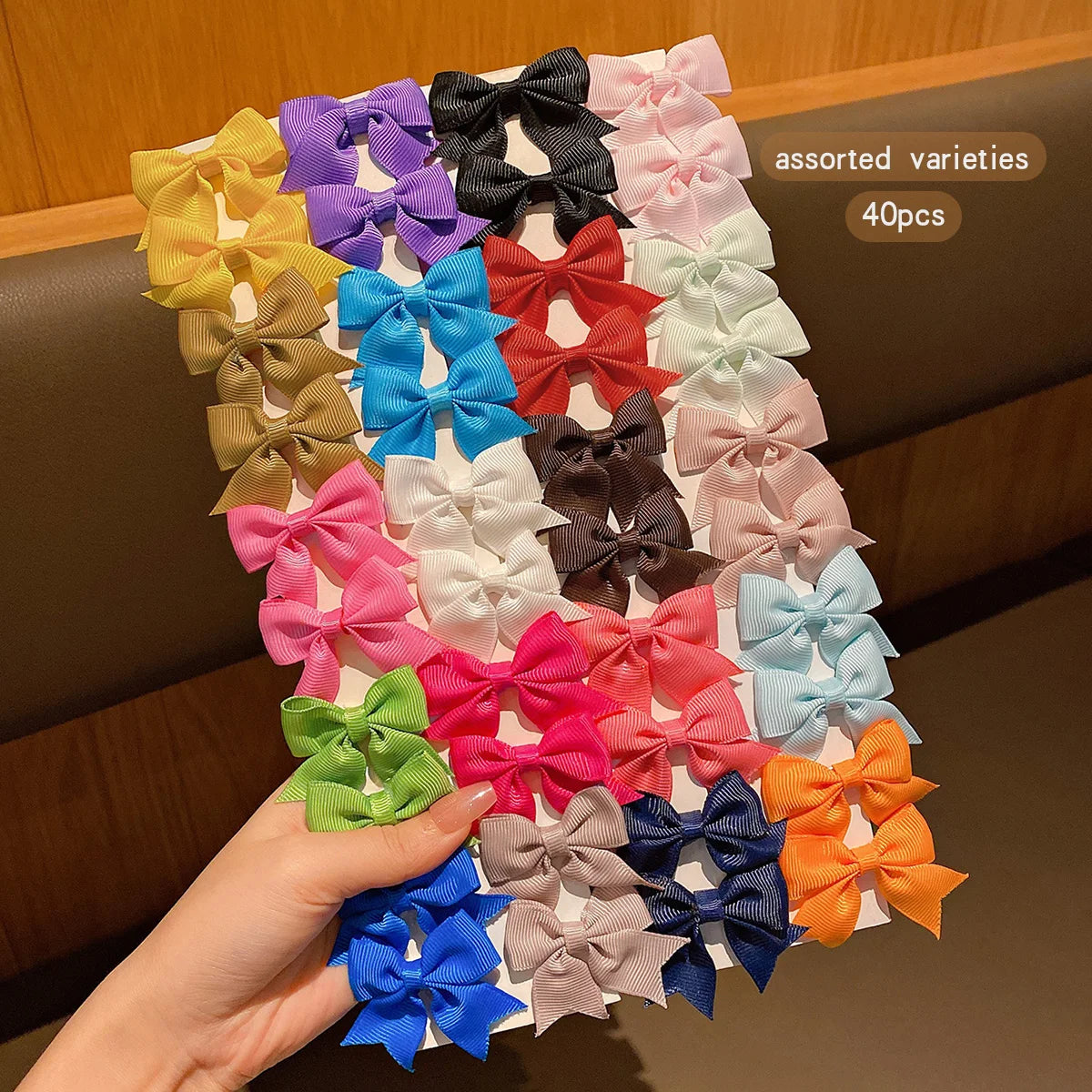 Assorted varieties of colorful fabric bows for hair clips, displayed on a wooden surface.