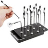 A hand holds a magnetic helping hands tool with a flexible gooseneck arm and alligator clip, positioned above a black tray of
