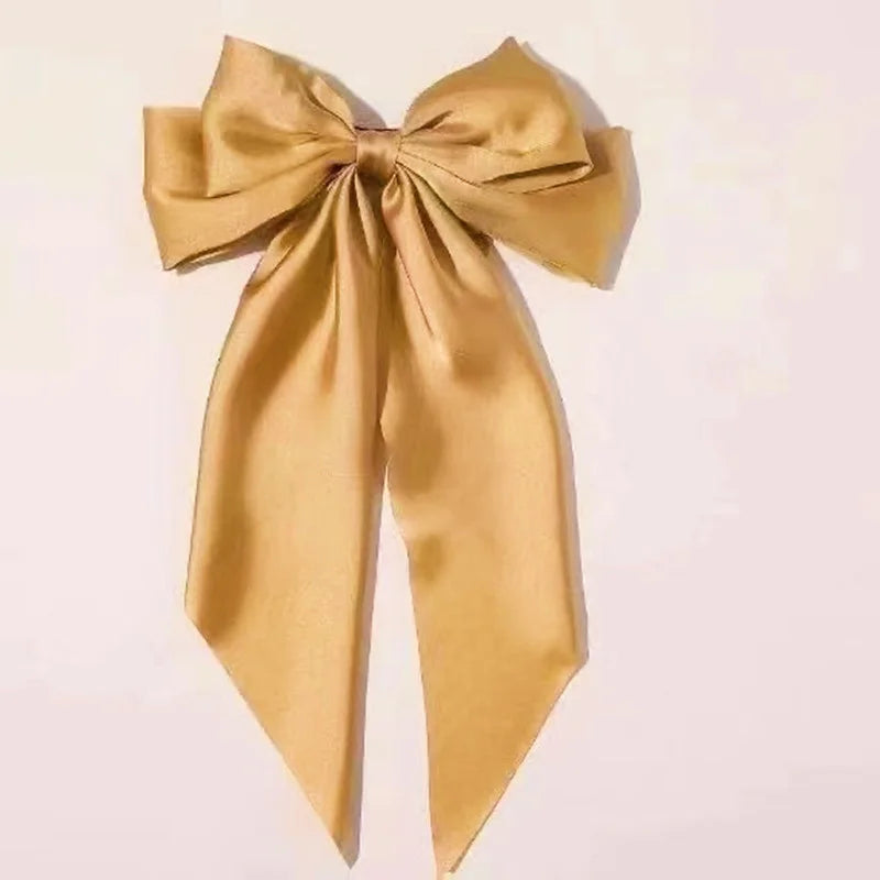A golden silk bow used as a hair clip or ponytail holder.