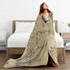 A woman is draped in a beige Middle Earth map fade-resistant plush throw blanket in a bedroom setting.
