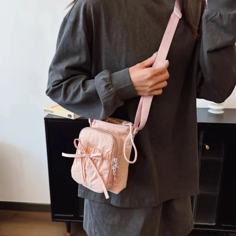A person holds a pink bow-decorated casual crossbody bag with an adjustable strap against a dark gray shirt.
