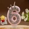 Pink number six candle with a rhinestone crown topper on a wooden surface