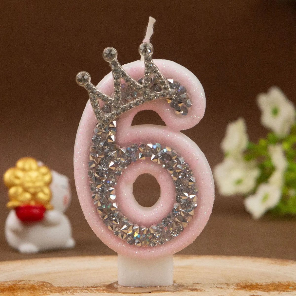 Pink number six candle with a rhinestone crown topper on a wooden surface