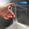 A hand is gripping a drain unclogging tool with a curved red handle inside a stainless steel sink.
