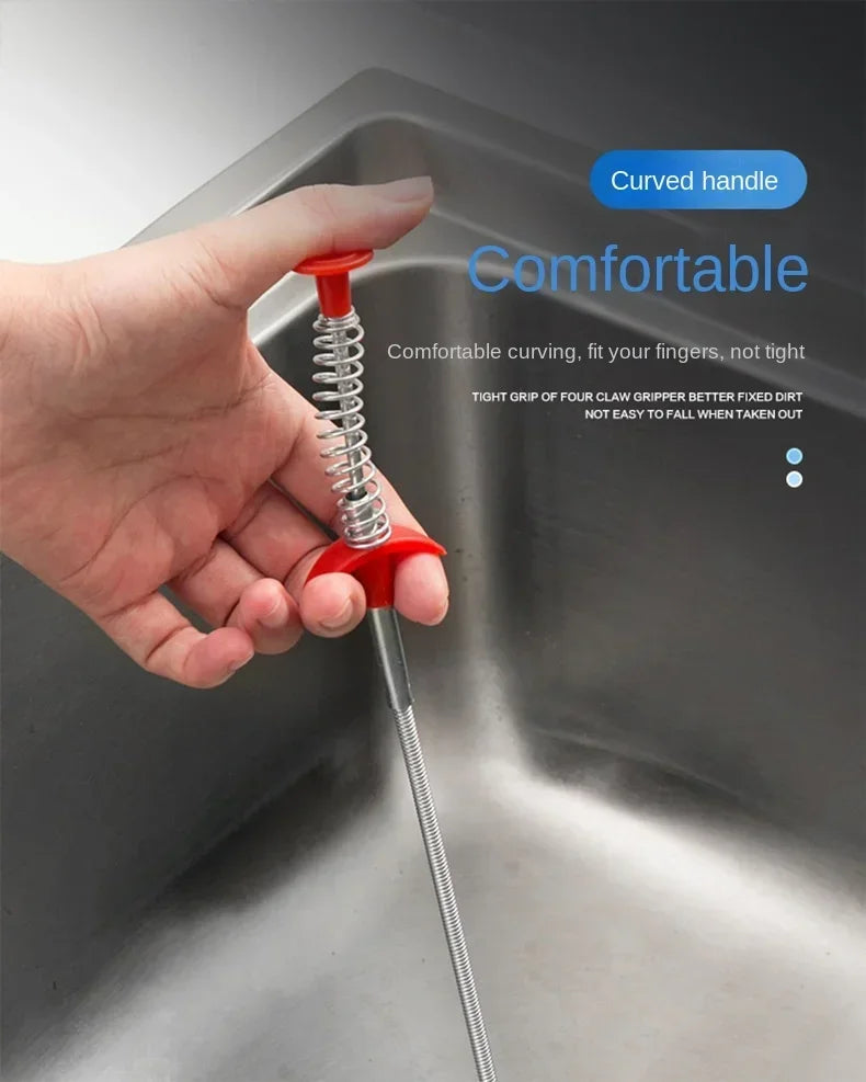 A hand is gripping a drain unclogging tool with a curved red handle inside a stainless steel sink.