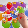 A hand is writing on colorful dry erase fly swat game cards for kids, featuring various fruit-themed designs.