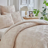 A beige duvet cover set with a delicate leaf print pattern displayed on a bed with pillows and a table lamp.