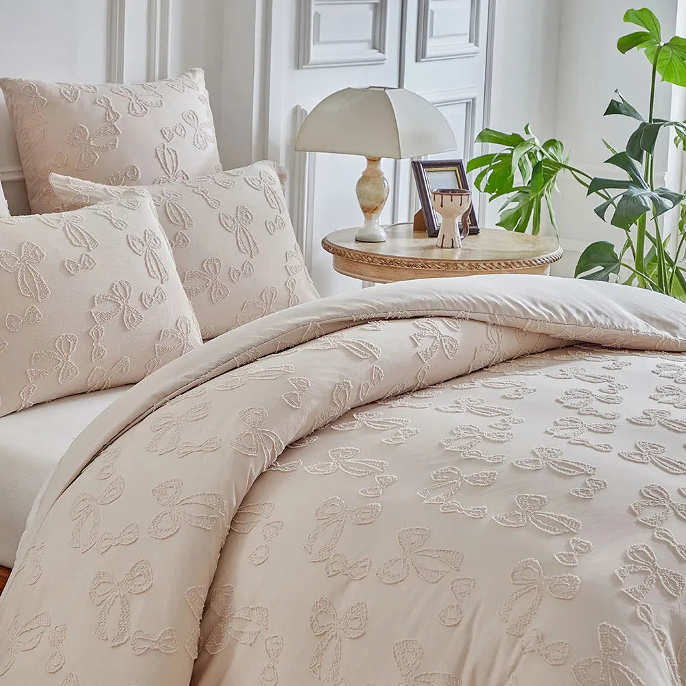 A beige duvet cover set with a delicate leaf print pattern displayed on a bed with pillows and a table lamp.